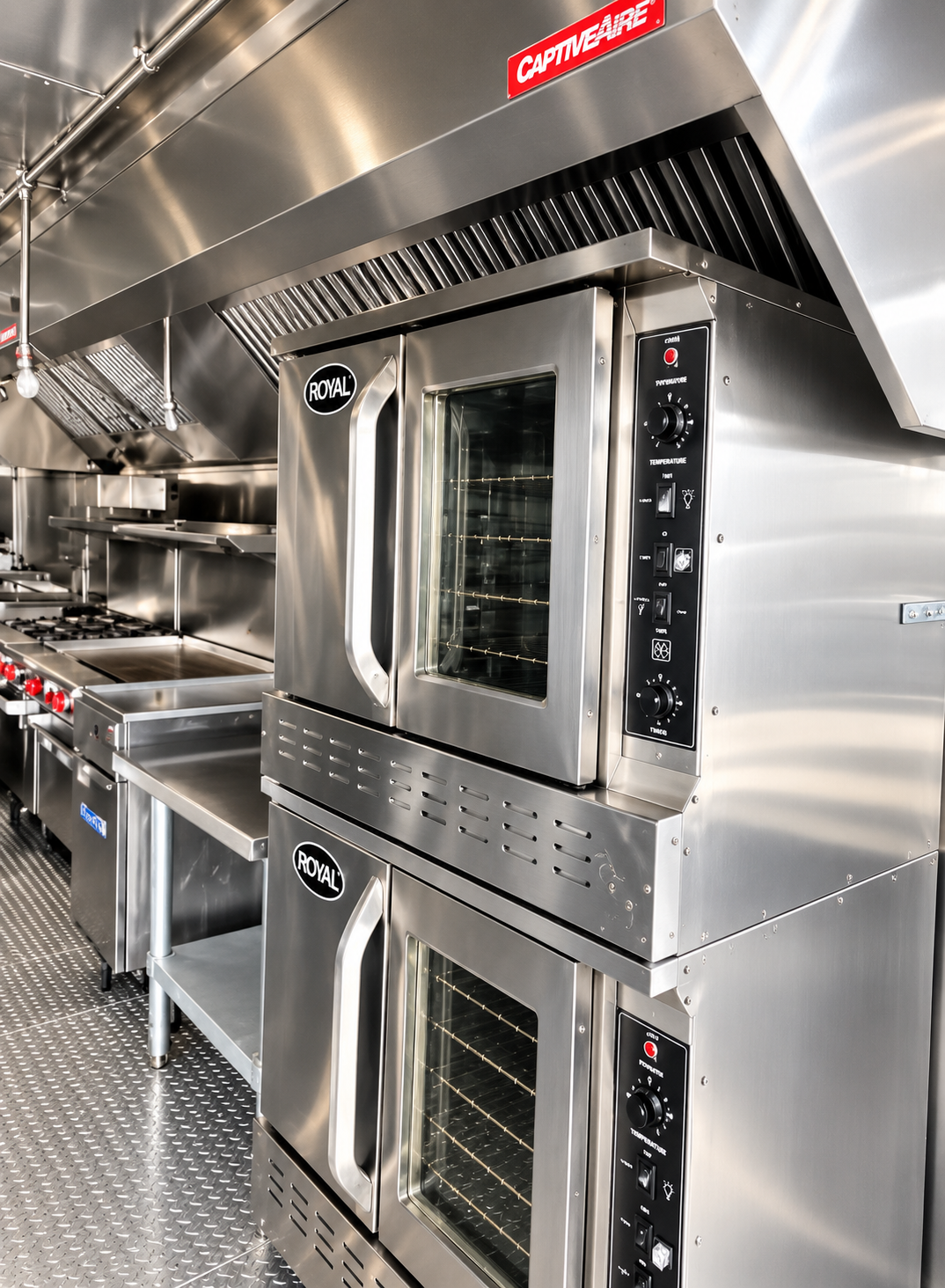 Two stacked ovens beneath a ventilation hood inside a mobile kitchen