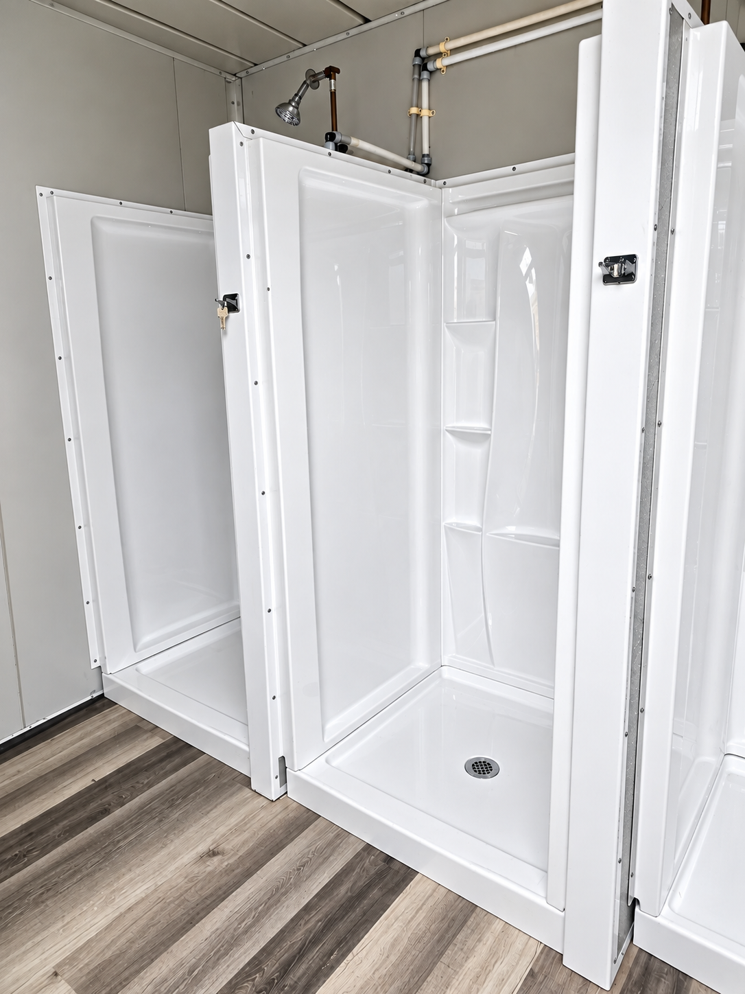 Several white shower stalls with doors and drains